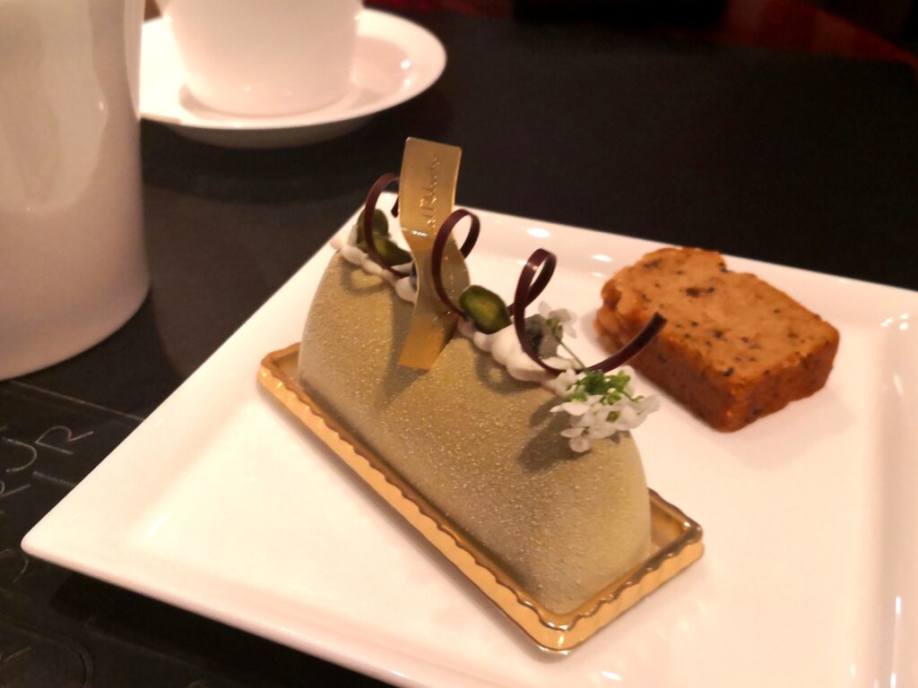 （ムース ピスターシュ グリオット）
淡い緑色のピスタチオムースのケーキ。金色のチョコ細工、ピスタチオ、白い花、チョコレートのリボンで繊細に飾られている