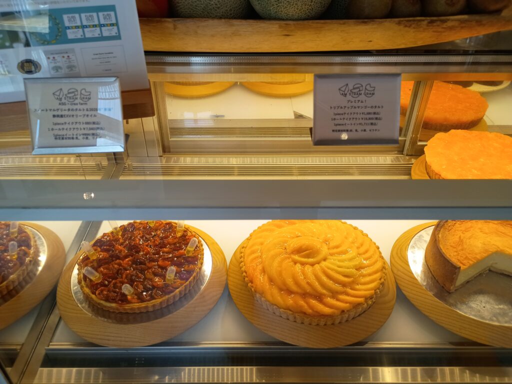 ショーケースに並ぶスイートマルゲリータのタルト（左）と、鮮やかなオレンジ色のトリプルアップルマンゴーのタルト（右）。奥の棚にはカットされたクリームチーズのタルトも見える
