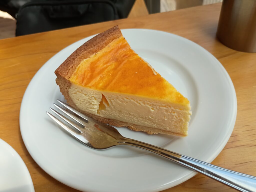 アムストラムグラムのクリームチーズのタルト、イートイン用の一切れ。こんがりとした焼き色のオレンジ色の表面と、なめらかなクリームチーズの白い断面が美しいコントラストを見せる。ボリューム感のある一品
