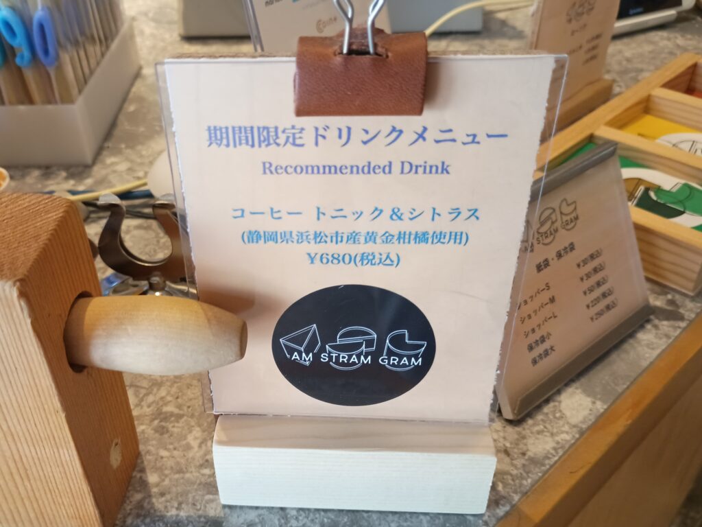 アムストラムグラムのカウンターに置かれた期間限定ドリンクのPOP。「コーヒートニック＆シトラス（静岡県浜松市産黄金柑橘使用）¥680（税込）」と青い文字で記載され、下部にはブランドロゴのステッカーが貼られている

