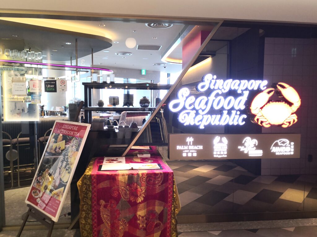 シンガポール・シーフード・リパブリック東京の入口。青く光るネオンの筆記体ロゴと赤いカニのマーク