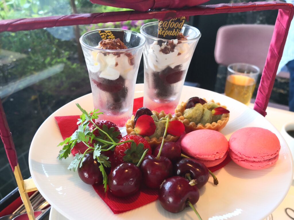 （上段）
上段の皿。生クリームを重ねたパフェ2杯、チェリー、いちご、ピンクのマカロン、抹茶のタルト