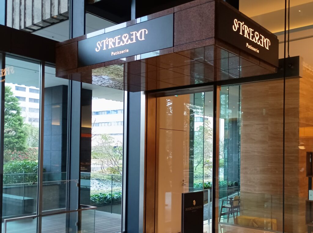 インターコンチネンタルホテル大阪内、パティスリー ストレスの入口。ダークブラウンのシックな看板に白い文字でSTRESSEDのロゴが輝き、ガラス張りの向こうには庭園が見える落ち着いた雰囲気