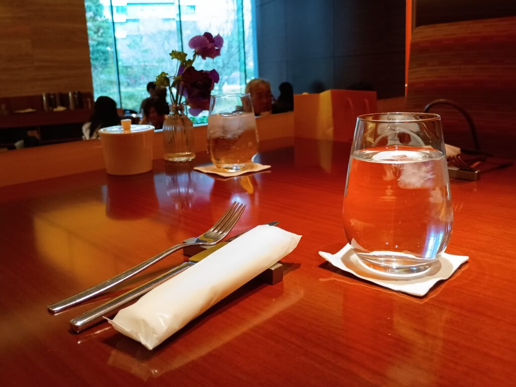 パティスリー ストレスのテーブルセッティング。木のテーブルに銀のフォークとナイフ、白いナプキン、水の入ったグラスが丁寧に並べられ、奥には紫の花の小さな花瓶が添えられている