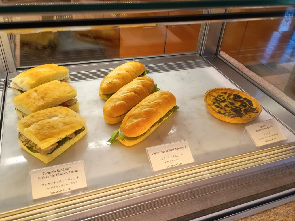 パティスリー ストレスのショーケース。フォカッチャサンドウィッチ(ハーブチキングリル、トマト)、フィリーチーズステーキサンドウィッチ、キッシュ(ローストベーコン、ほうれん草)が並ぶ